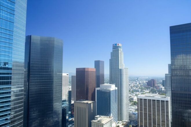 Prise de vue aérienne de la skyline de Los Angeles avec des gratte-ciels modernes sous un ciel bleu clair, mettant en valeur la beauté urbaine.
